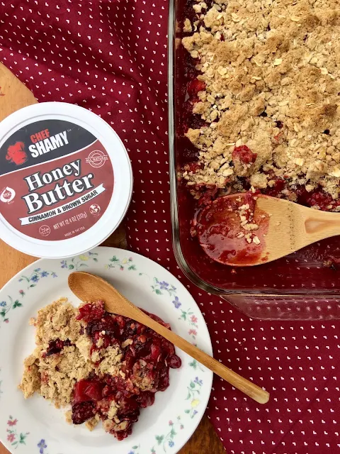 Honey Cinnamon Summer Berry Crisp in a baking dish with some scooped onto a serving plate.