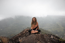 A women in a lotus position with her eyes closed at the top of a hill