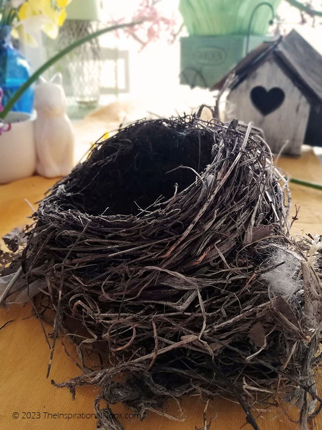 Old robin's nest on table with a heart bird house in background, reusing a bird nest,