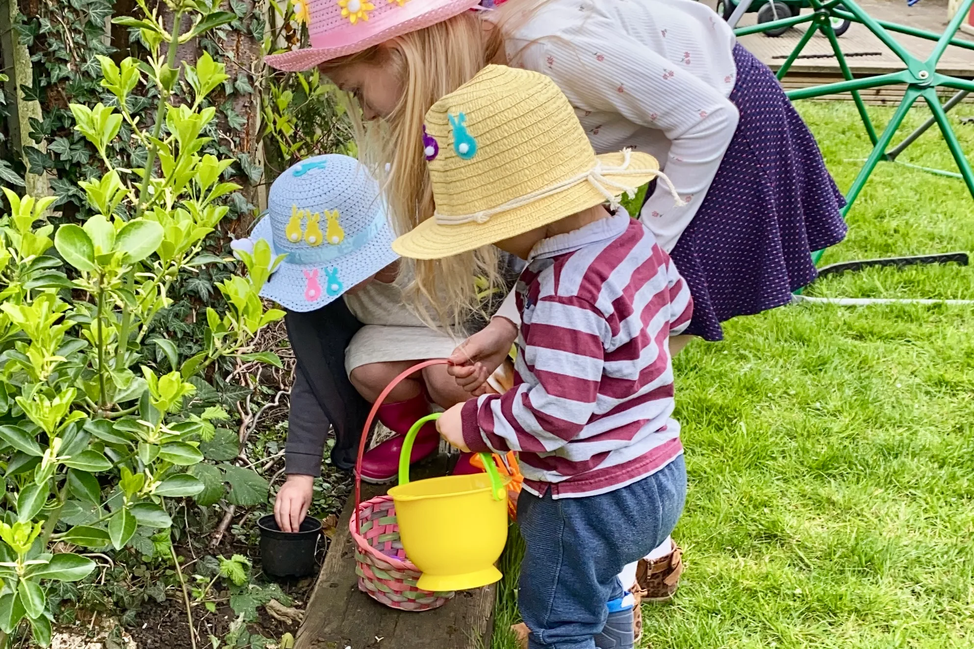 3 children with baskets and Easter bonnets looking for Easter eggs