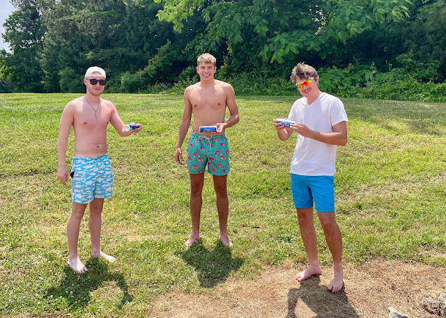 Ryan, Josh, and Andy standing in the grass getting ready to chug a beer beside the lake.