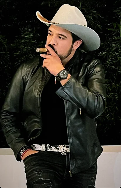 Handsome cowboy with a white hat on wearing black leather jacket and smoking a cigar outside on porch