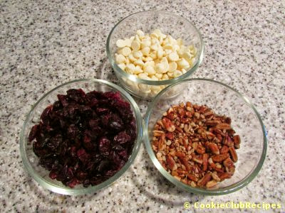 glass bowls of white chocolate chips, dried cranberries, pecans