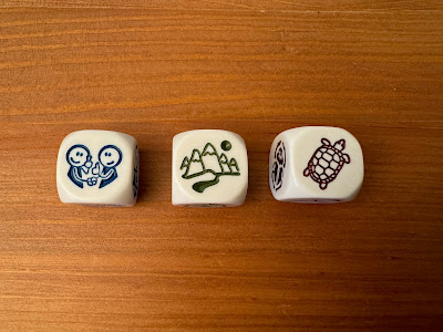 three story cube dice: two people shaking hands giving thumbs up; mountains with a river and moon; a tortoise or turtle