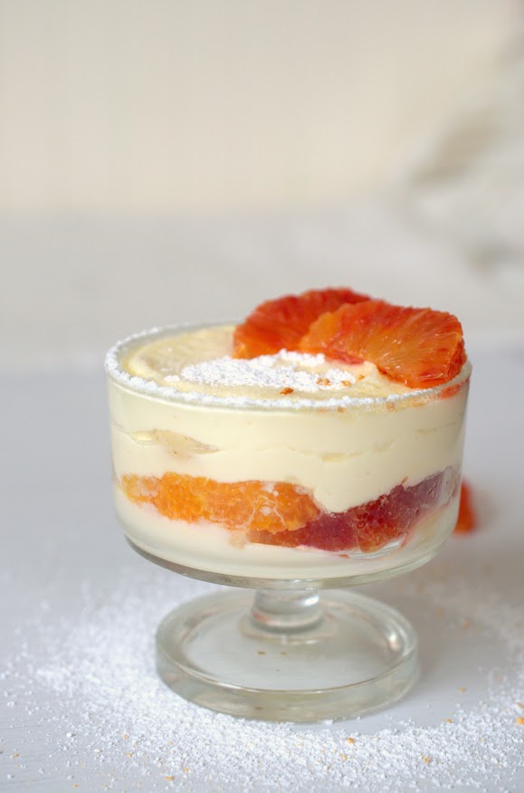 Blutorangen-Tiramisu ist in einem kleinen Glas geschichtet. Man sieht die leuchtenden Blutorangen-Filets. Die Oberfläche des Desserts ist mit Staubzucker bedeckt.