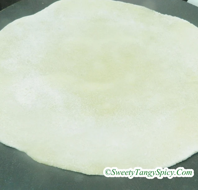 Chapati dough circles placed on a hot tawa, sizzling and puffing up during the cooking process.