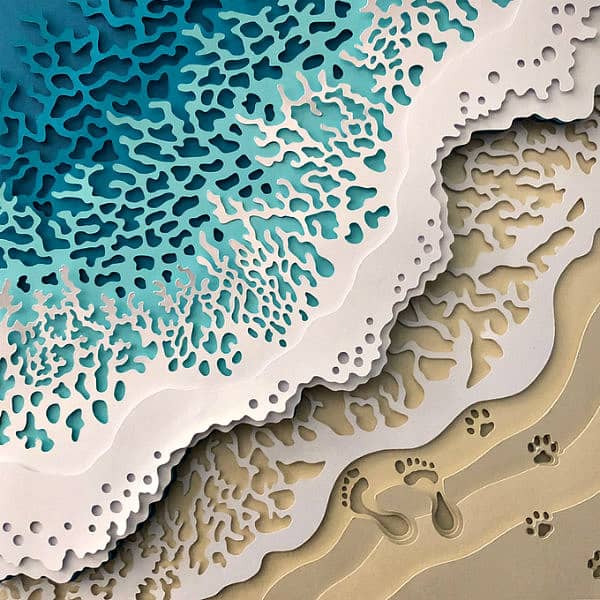 layered paper cuttings of beach and foamy waves with human and dog footprints in the sand