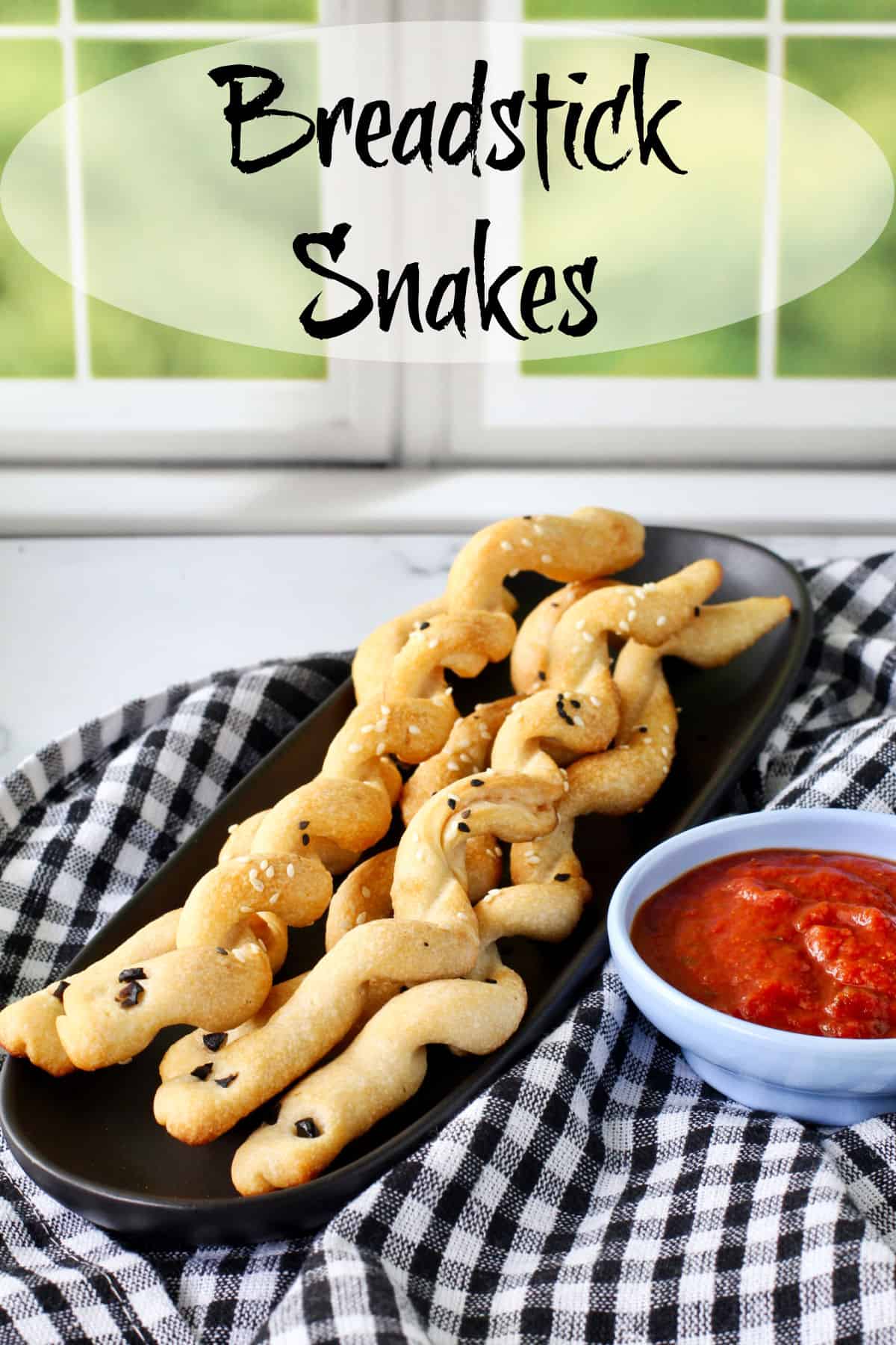 Breadstick Snakes on a black plate with dipping sauce.