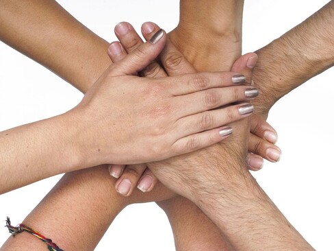 Seven hands, male and female, white, stacked atop each other seemingly in solidarity