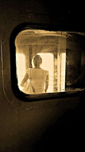 Девушка в тамбуре электрички, собирается выходить на станции Ржевская. Около-железнодорожное. Фотография черно-белая сепия грязное стекло темный светлый двери вагон