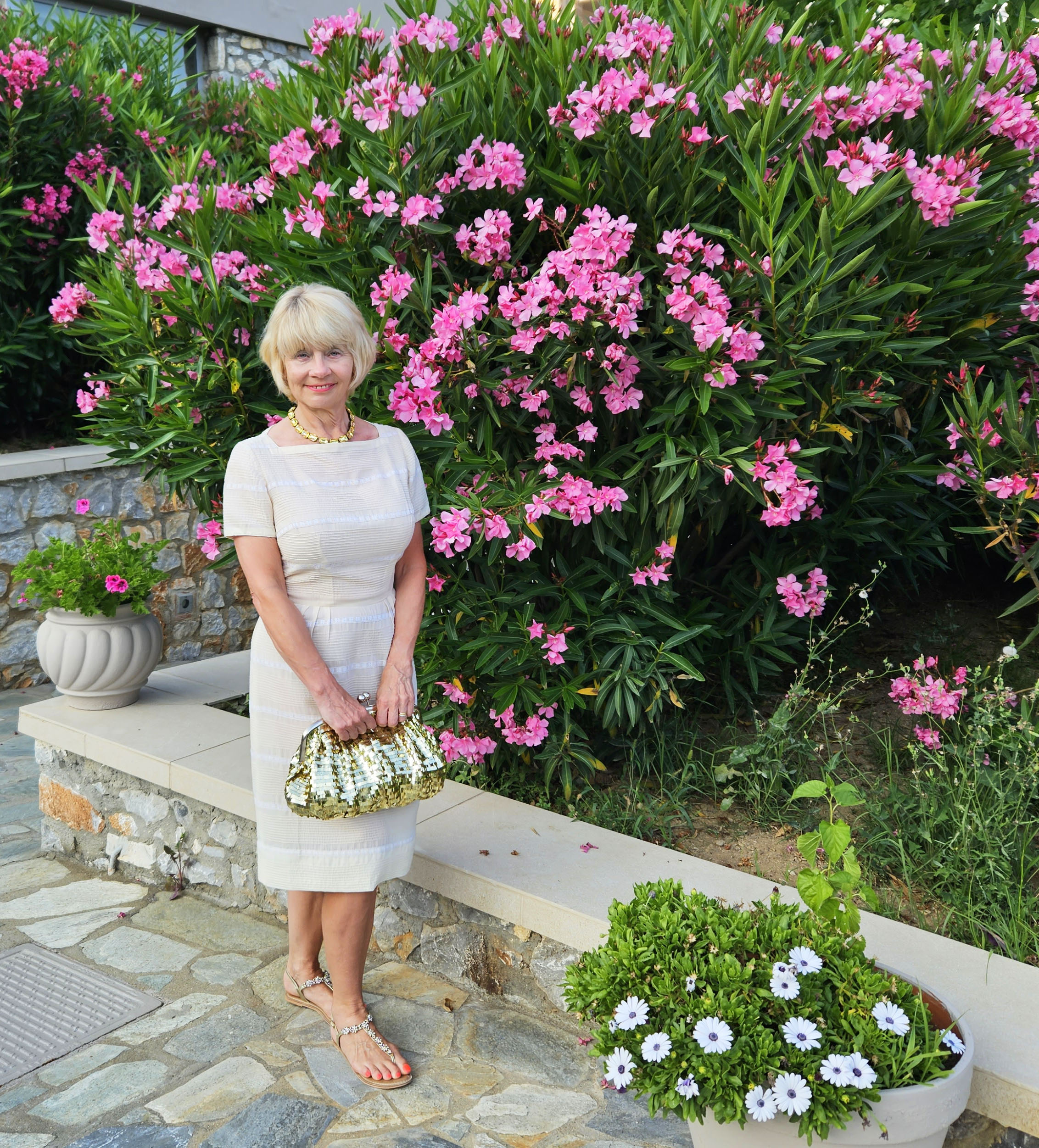 Gail Hanlon on holiday in Greece wearing a cream cotton dress and backed by bougainvillea