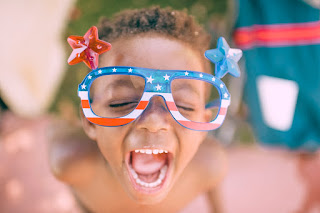 Close-up of a child laughing and wearing red, white & blue glasses with stars on the top. Photo by Frank McKenna on Unsplash.