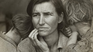 Black and white photo of an adult woman gazing melancholically in the distance with her children clutching onto her.