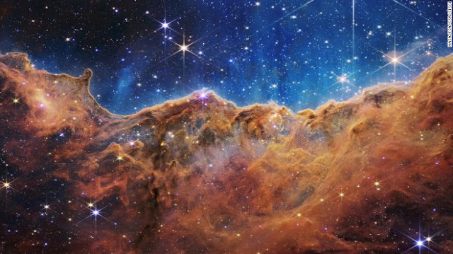 Ayoung, star-forming region called NGC 3324 in the Carina Nebula. Brown clouds under blue firmament speckled with stars.