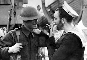 A British soldiers gives a light to a Canadian sailor, January, 1941.