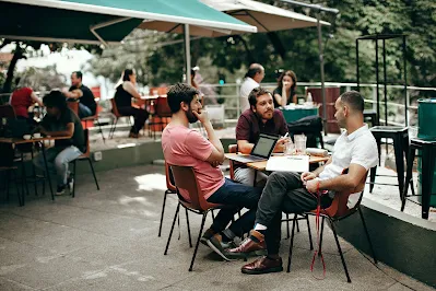 Three men sit around a laptop outside a cafe