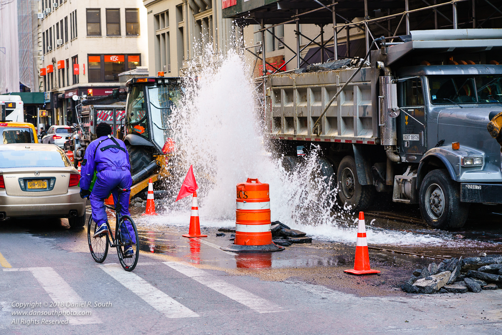 a photo of a cyclist riding past a water main break in new york city