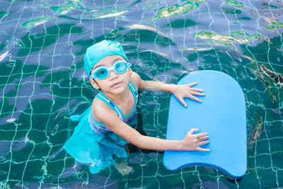 image from above of little girl in the pool holding a kick board looking up