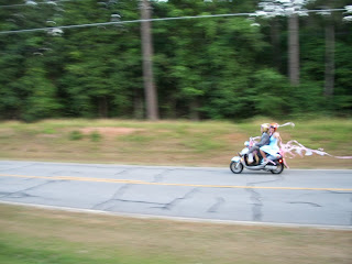 Bride and groom zoom down the road on a scooter with streamers trailing.