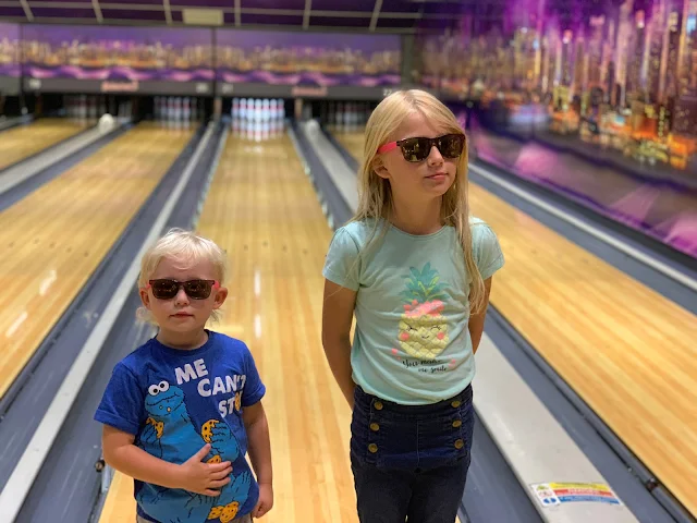 2 girls posing in sunglasses in front of bowling alleys