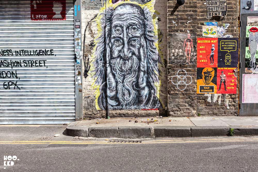 Large-scale black and white hand-painted paste-ups on Fashion Street featuring an elderly bearded man