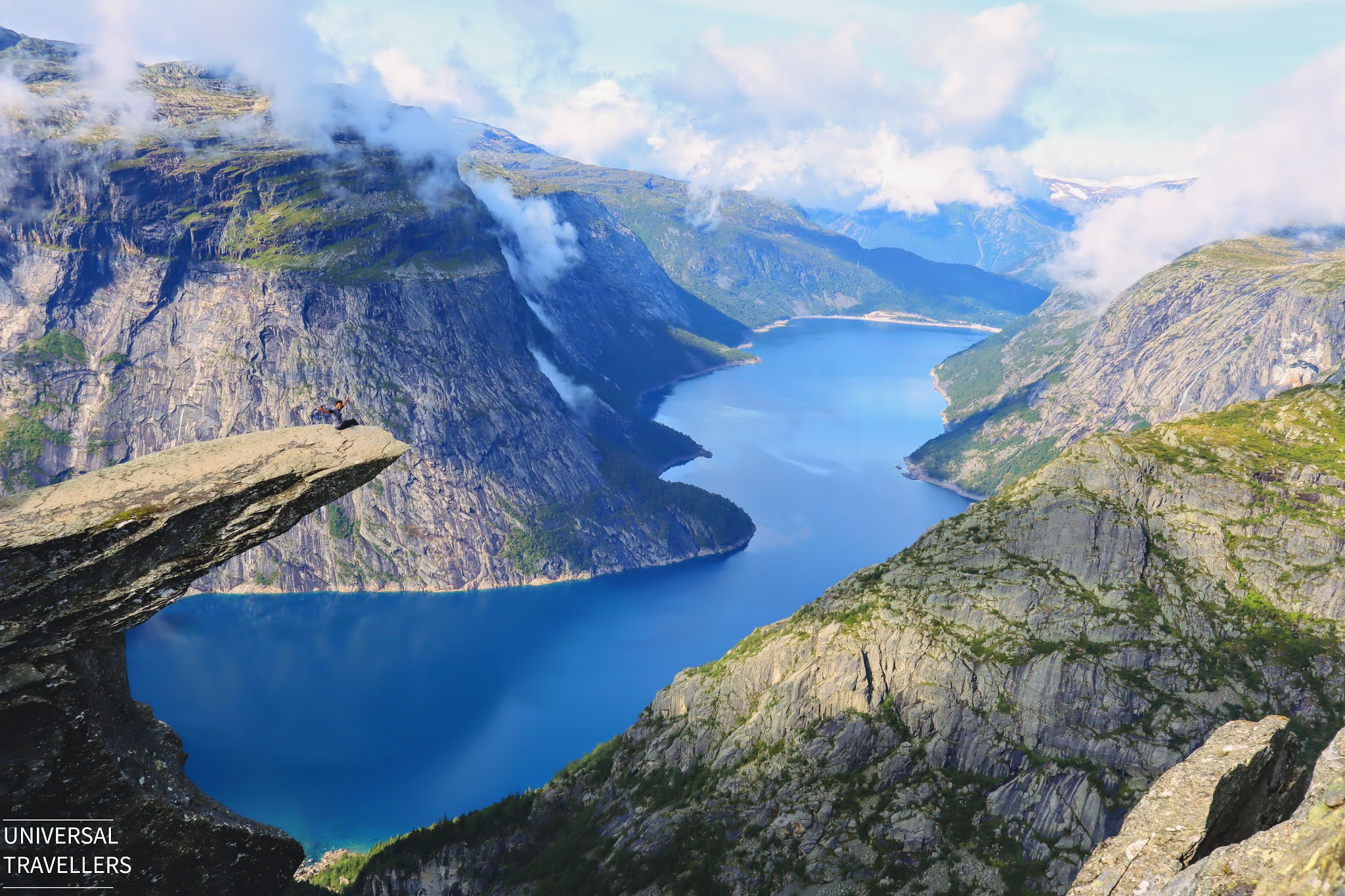 A boy is sitting at the edge of Trolltunga Cliff posing for the camera