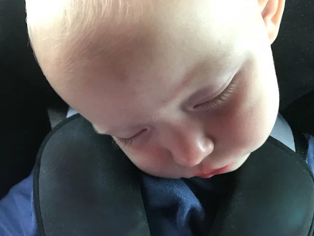 A close up of a toddler asleep in a car seat with her head at an angle