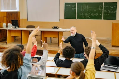 Seorang guru mempersilahkan salah satu siswanya yang mengacungkan tangan di dalam kelas