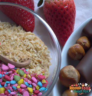 Image of the ingredients. A bowl with strawberries, a chocolate bar, sprinkles and chopped nuts. 