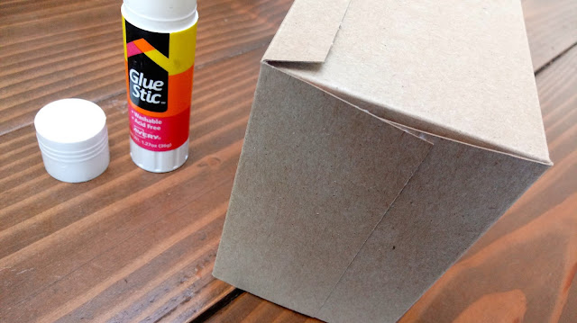 a cardboard box glued inside out sitting on a table next to a glue stick