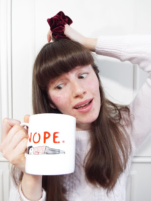 Ellie depicting the absolute image of stress, scarcely holding up a cup of tea in a Gemma Correll mug, with the word "nope" written across it, with imagine of a lady lying on floor; attempting to tie hair up in bobble; and sporting a stressed expression