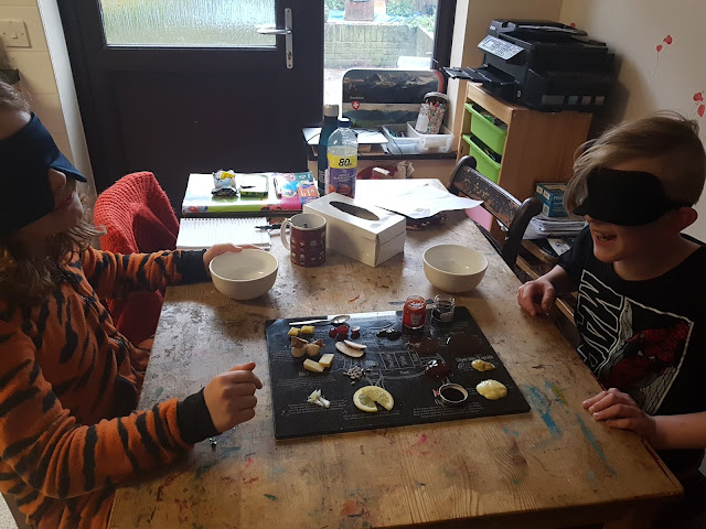 The two boys sat smiling excitedly at the table with the food in the middle of them. Both blindfolded and laughing.