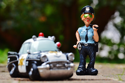 Policeman wearing sunglasses holding baton standing with his car