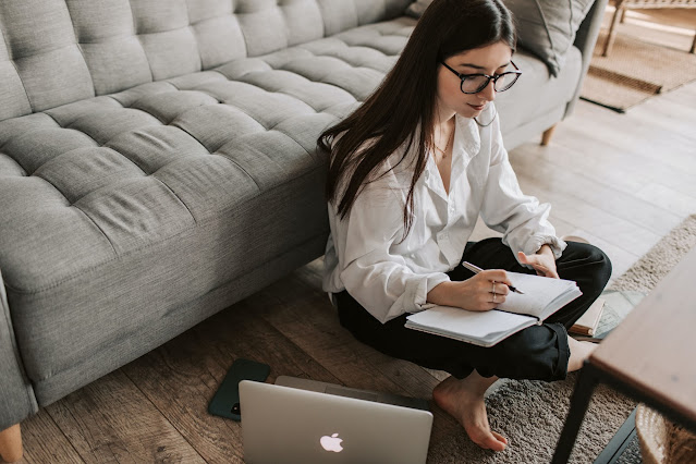 A lady writing in a book with Macbook beside her
