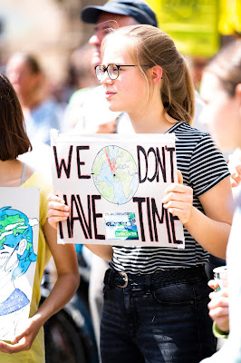 a girl with a poster in her  hand in which the word "we don't have time" written in academic pressure image