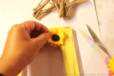 Hand hold paper yellow sunflower to yellow frame near a bundle of twine