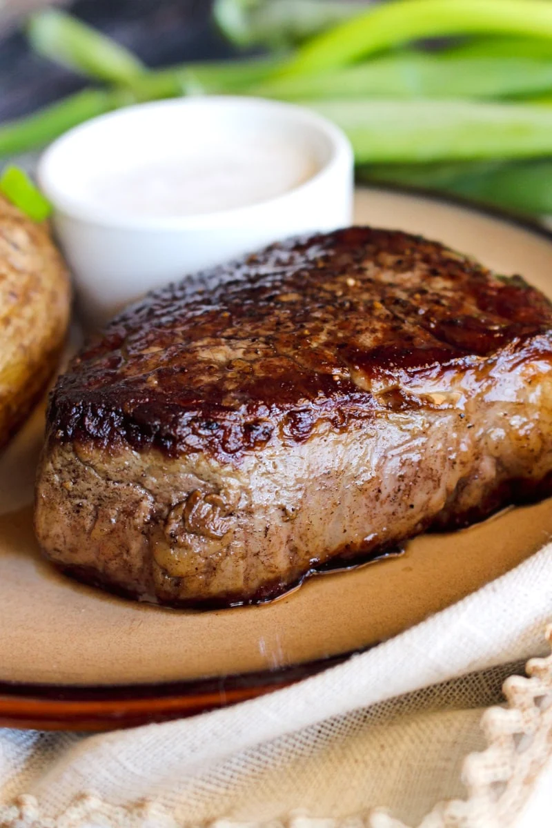 Seared filet mignon on a brown plate with a small white cup of horseradish sauce behind it.