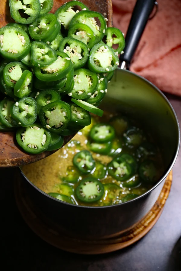 In the process of making cowboy candy, sliced jalapenos are being added to the pot filled with a flavorful syrup mixture. The combination of heat from the jalapenos and sweetness from the syrup promises a delectable candied treat.