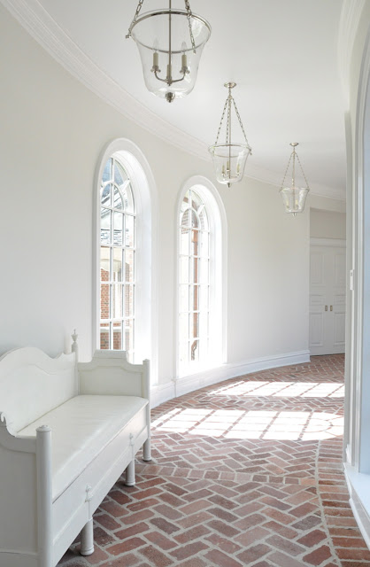 kathleen clements' curved hallway with arched windows, brick floor laid in a herringbone pattern, lanterns and white walls