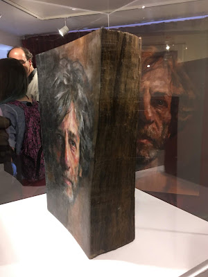 photo of display case holding a wooden book, on the cover of which is painted a portrait of Neil Gaiman