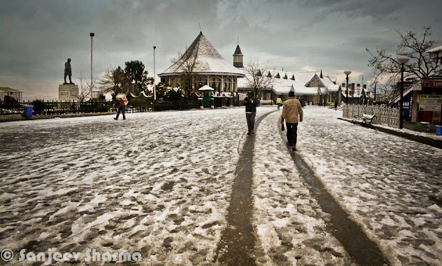 Shimla has been getting snowfall since 5th January 2012 and Sajeev has been capturing each moment of post-snowfall moments at various places around Shimla - Mall Road, Ridge ground, Scandal point, Lakkar Bazar etc. This year Shimla is getting heavy snowfall and some of the evidences can be seen in this Photo Journey from last week... Sanjeev Sharma with unknown Cameraman, Zee news, Shimla :)Sanjeev himself on Ridge Ground, while it's snowing on Ridge Ground, Shimla, Himachal Pradesh, India. You can see Christ Church on one corner of the Ridge and Shimla Library adjacent to it. Somehow Shimla is known by these two buildings. Yesterday only I saw fridge magnet at Connaught Place, Delhi with these two buildings carved on a marble piece to make a souvenir of Shimla, Himachal Pradesh. There were lot of other stuff form various cities of India like Jaipur, Varanasi, Maisoore etc.Here is a photograph with footmarks of people who were enjoying fresh snowfall on Ridge Ground and left for their homes.Although there are still few folks roaming around. Whole sky is covered with dense mist or clouds. The leading path is actually touching Mall Road, which is one of the main places people love to roam around in Shimla. buildings on left side are Goofa Restaurant and Bar by HPTDC and Gaitey Theatre, which was renovated last year only.Here is a closer look to Goofa Restaurant and Bar. One of the decent place to have dinner on Ridge Ground, although our experience of Goofa bar was not so good, when we were in University. But this is considered one of the decent places..Business in Snow... The famous Krishna bakers is closed but 100 Pipers and other brands of whiskey are available. And probably Rum would be more demand in such a lovely snow. Just notice the height of snow on the road... All these shops are located on lower part of the Mall Road...Another view of ridge Ground from an elevated boundary which leads towards Jakhu Temple, Shimla.Snow was on and off during last 10 days and yesterday there was heavy snowfall, which made people comment negatively about it. Till yesterday everyone from Shimla was putting happy and interesting statuses about Snowfall on facebook. But suddenly things changed yesterday when this snow started impacting lives of people in Shimla. For tourists, heavy snowfall can be good but for loacl folks it creates lot of problems at times. Water and Electricity supply is one of the main challenge during heavy snowfall hours. Notice the forest behind Mr. Sanjeev which are still white and these high deodars look amazing with snow on top of themPath created by Ambulance is being smartly used by these folks. vehicles are not allowed on Ridge Ground and Mall Roads.. Only Ambulance or police vehicles are allowed as and when required. Although many bollywood movies have shown vehicles flying on ridge ground. All that is done after special permissions from Shimla Authorities.Here is a a view of Shimla Ice Skating Club, which is located just below Lakkar Bazar, Shimla. This club is also visible from top of Indira Market on Ridge Ground. During December a national level event is organized, where lot of professionals come to this club for showing their Ice Skating performances. Even without ice these folks from Shimla can be seen on Mall Road and Ridge on  every Saturday :)Evening view of Ridge with spoiled snow... Place like Shimla are enjoyable either during fresh snowfall or without any snow. After 2 or 3 days of snowfall, snow melts or take a shape of huge pieces of ice which are risky to walk and dirty as well. During that time, snow in places are Kufri or Narkanda is more enjoyable. In fact, these days Skiing training is going on at Dhomri, Narkanda...Mr. Sanjeev, covered with multi-layered cloths and posing for a photograph against scandal point. Scandal point is a place from where two roads are diverted - one towards Ridge ground and other continues as Mall Road towards Shimla Town Hall and Gaiety Theatre.Gukli just stood up for this photograph, otherwise he must be busy in making snowman or playing snowballs :) ... Smile on his face is telling about the excitement about fresh snowfall in Shimla.Every year tourists come to Shimla during last week of Decemeber in a hope of Snowfall, but now timings have shifted a bit. For last few years, Shimla is getting snowfall in second week of January or towards end of first week.This year (2012), it was first time that some of the regions in Himachal got snowfall. Places like Hamirpur were also covered with white sheet of snow, although it remained only for few hours and then disappeared. At the same time various places of Kangra District got snowfall - Nagrota, Palampur, Dharmshala and Kangra town itself. Kangra Twon got snowfall after 52 years...Sanjeev is still waiting for his car to be uncovered of Snow Blanket... Try to imagine, how people in Shimla must be commuting to their offices and other places for some work... Conditions get worse in case of continuous snowfall for longer period of time.Many businessmen in Shimla make more money during tis season but at the same time, many folks with small setups loose lot of business due to heavy snow. I am sure that every weekend Shimla is getting lot of tourists from Punjab and Delhi...Sanjeev in perfect pose for this photograph with snow in the background :) (Shimla, Himachal Pradesh, India)Another amazing view of Ridge Ground covered with Snow and few folks walking on it... I still remember the day when I saw snowfall first time and we came to Mall Road for playing with snowballs... Everyone from our class was on Mall Road and whole day was full of fun and enjoyment....Sanjeev looks pretty happy and hopeful about this snowfall... Probably he is done with his walk on Mall Road and moving towards Press Club at Indira Market on Ridge ground of Shimla TownHere is last and wonderful photograph of this amazing Photo Journey by Sanjeev Sharma. Hope that snowfall comes with happiness and keep whole environment cheerful without any damage to anyone. And if you are amongst ones who have never seen snowfall, this is right time to plan your trip to Shimla and enjoy it.Thanks a Lot Sanjeev Sharma for such a Lovely Photo Journey with full of life photographs from last one week.