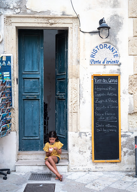 Niña con camisa amarilla sentada en una puerta azul comiendo un helado