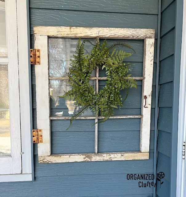 Photo of a chippy window frame hanging by the front door with a wreath.