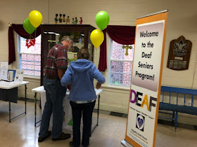 two people look at a table,  on their right is a banner, "Welcome"