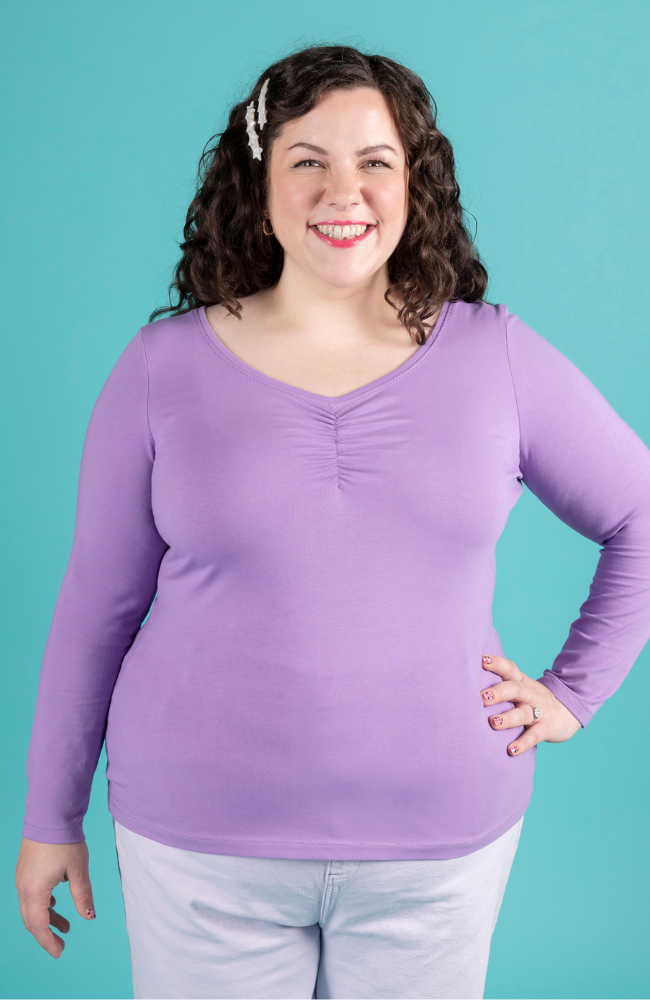 Model with brunette curly hair wears purple long sleeve jersey top with sweetheart neckline