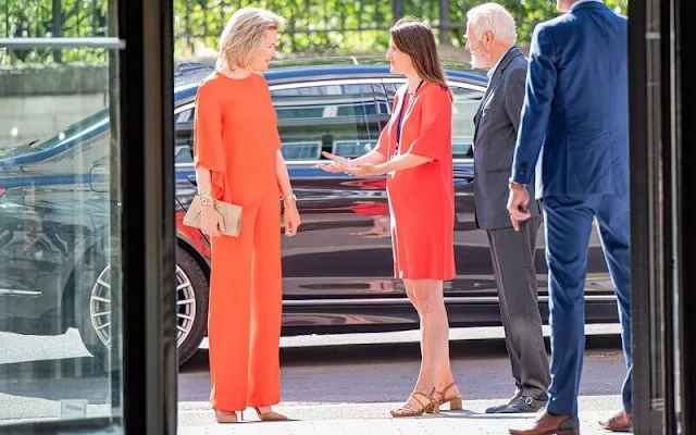 Queen Mathilde wore an orange Adria asymmetric jumper by Natan, and orange Milan trousers from Natan. Gold earrings