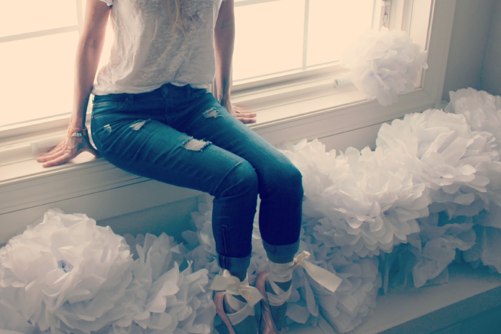 Michele of Hello Lovely Studio in pink pointe shoes and jeans at window with white tissue poufs