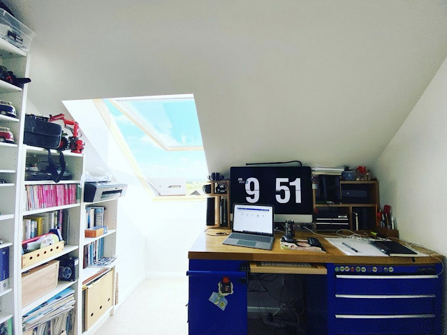 View of my desk.  Shelves on the left.  Open laptop and Mac with Time screensaver