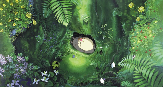 Film still from My Neighbour Totoro. An overhead shot of the forest, where Mei is lying on Totoro stomach.