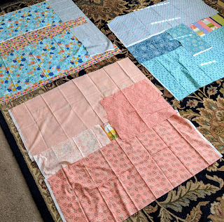 Three small tops are laid out so backing fabric can be properly sized. The fabrics are grouped by color to create monochromatic backs in blue or peach.